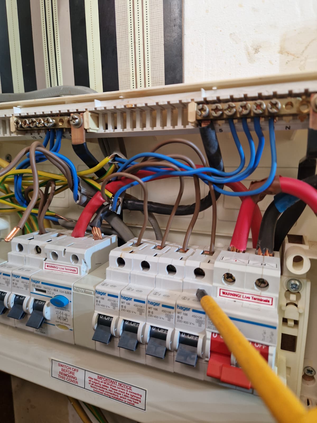 Opened Hager consumer unit showing tangled live, neutral and earth wiring with a pencil pointing to a circuit breaker terminal